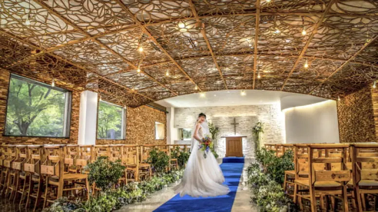 青いバージンロードと木製の椅子が特徴的なナチュラルなチャペルでの結婚式の風景